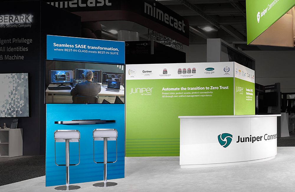JuniperDemo Juniper Networks trade show booth with branding, informational panels on SASE and Zero Trust, two stools, and counter on a convention floor.