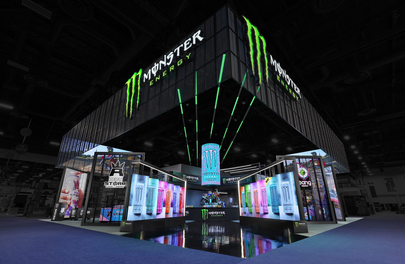 A large Monster Energy booth with illuminated signs, digital screens, and product displays at an indoor event or trade show.