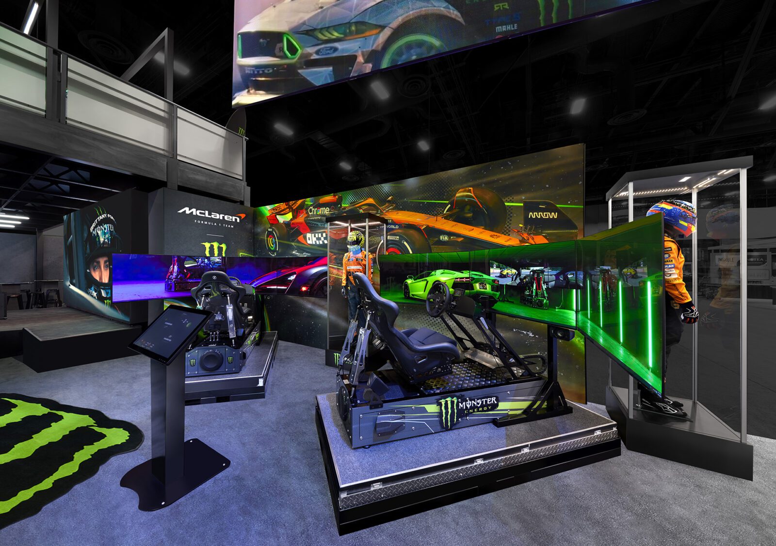Two racing simulator setups with curved monitors are displayed in a vibrant, motorsport-themed exhibit with McLaren and Monster Energy branding.