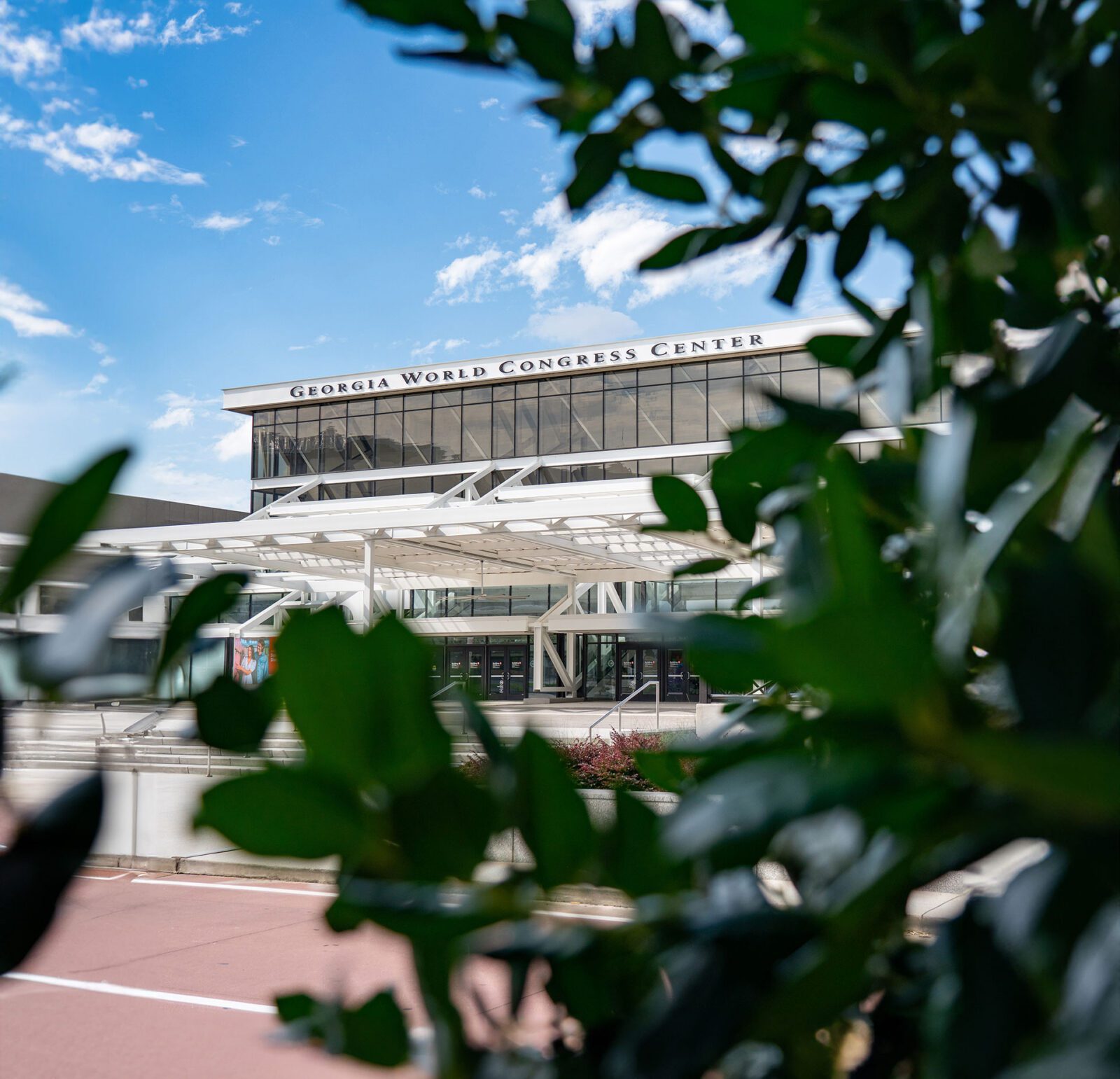 View of the Georgia World Congress Center building, partially framed by green leaves in the foreground under a blue sky.