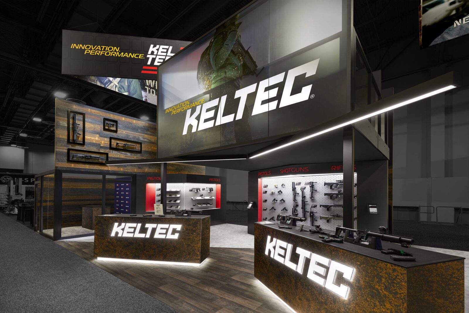 KELTEC trade show booth displaying firearms and accessories with illuminated company logos and large overhead signage.
