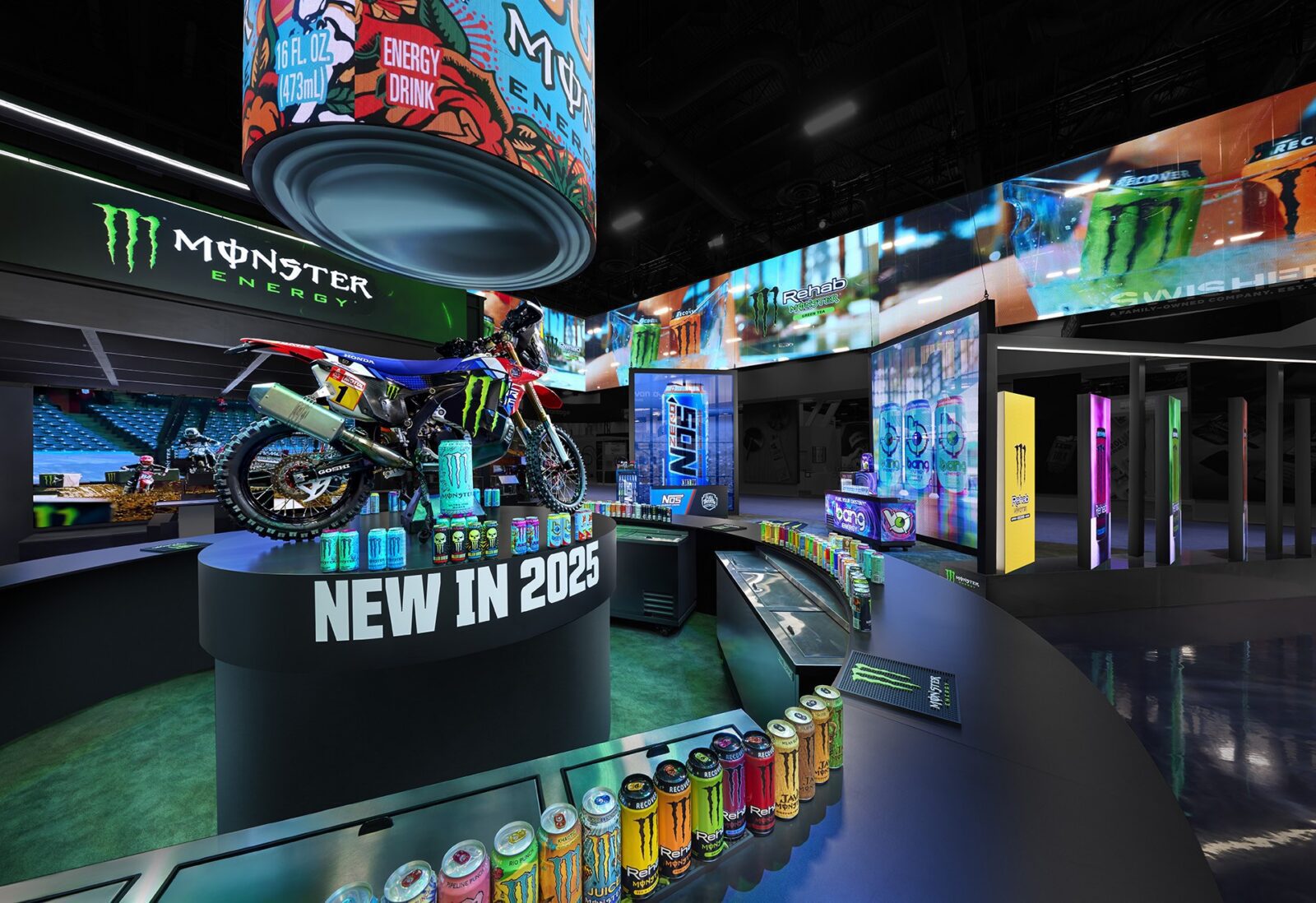 An indoor display showcases Monster Energy cans, a motorcycle, and signs announcing “New in 2025,” all thoughtfully arranged as part of an innovative trade show design, with colorful lights and digital screens illuminating the background.